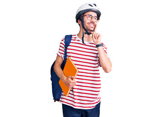Young hispanic man wearing student backpack and bike helmet holding binder serious face thinking about question with hand on chin, thoughtful about confusing idea