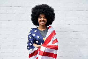 Happy young African American woman with Afro hair standing on white background wrapped in USA flag...