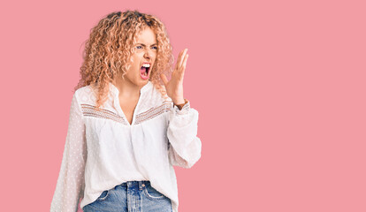 Young blonde woman with curly hair wearing elegant summer shirt shouting and screaming loud to side with hand on mouth. communication concept.