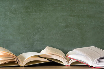 Open books against green chalkboard, close up