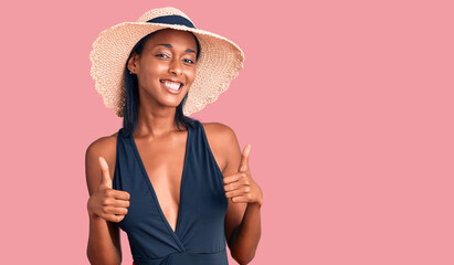 Young african american woman wearing swimsuit and summer hat success sign doing positive gesture with hand, thumbs up smiling and happy. cheerful expression and winner gesture.