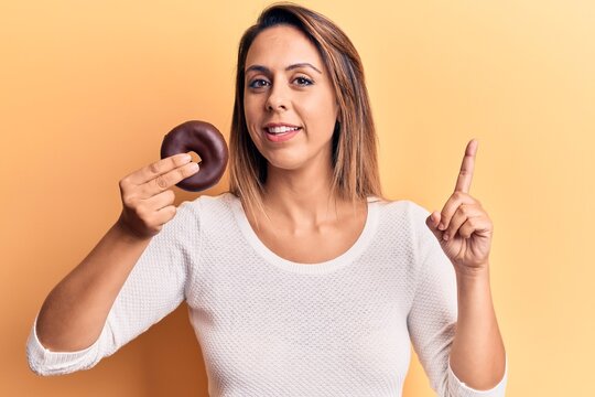 Young beautiful woman holding donut smiling happy pointing with hand and finger to the side