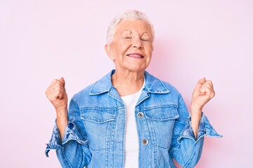 Senior beautiful woman with blue eyes and grey hair wearing casual denim jacket very happy and excited doing winner gesture with arms raised, smiling and screaming for success. celebration concept.