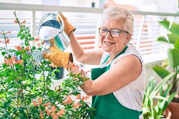 Senior woman with grey hair wearing gloves and gardener apron gardening the plants at home