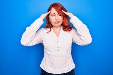 Fototapeta premium Young beautiful redhead businesswoman wearing elegant shirt standing over blue background with hand on head, headache because stress. Suffering migraine.