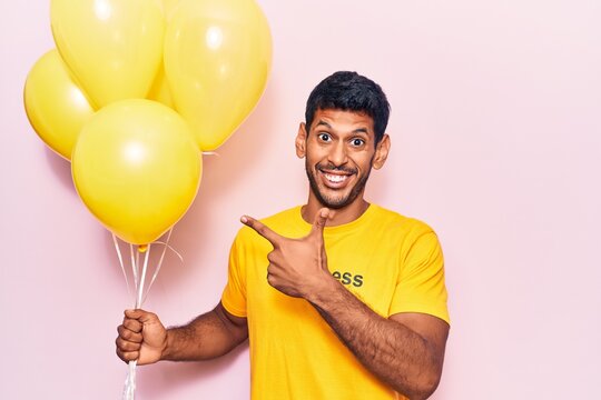 Young latin man wearing t shirt with happiness message holding balloons smiling happy pointing with hand and finger