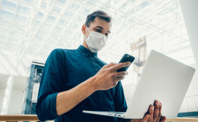 young man in a protective mask is choosing a contact in his smartphone