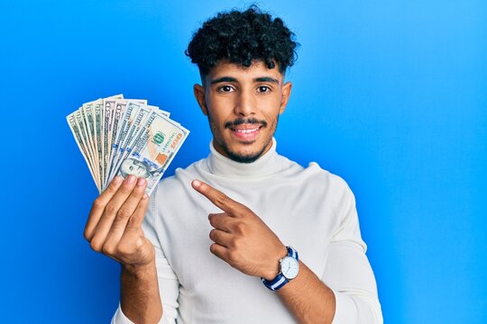 Young arab handsome man holding dollars smiling happy pointing with hand and finger