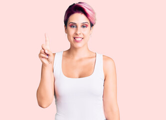 Young beautiful woman with pink hair wearing casual clothes showing and pointing up with finger number one while smiling confident and happy.