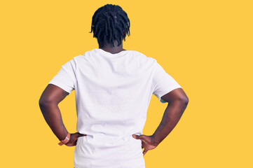 Young african american man with braids wearing casual white tshirt standing backwards looking away...