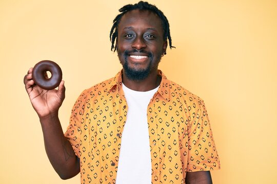 Young african american man with braids holding donut looking positive and happy standing and smiling with a confident smile showing teeth