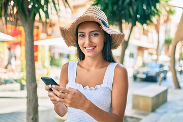Young latin girl wearing summer style using smartphone at street of city.