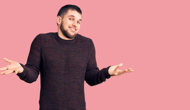 Young handsome man wearing casual sweater clueless and confused expression with arms and hands raised. doubt concept.