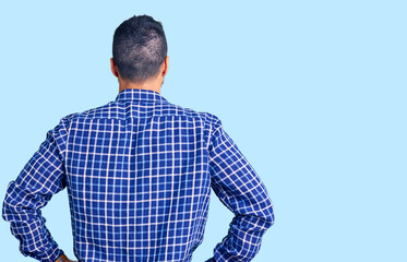 Young hispanic man wearing casual clothes standing backwards looking away with arms on body