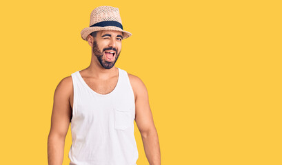 Young hispanic man wearing casual summer hat winking looking at the camera with sexy expression,...