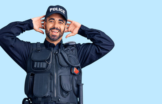 Young hispanic man wearing police uniform relaxing and stretching, arms and hands behind head and neck smiling happy
