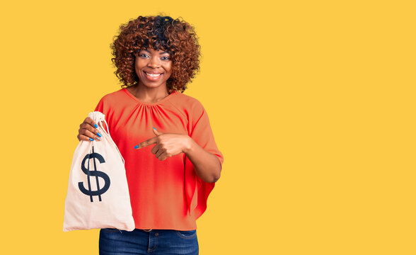 Young african american woman holding money bag with dollar symbol smiling happy pointing with hand and finger