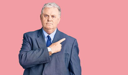 Senior grey-haired man wearing business jacket pointing with hand finger to the side showing advertisement, serious and calm face