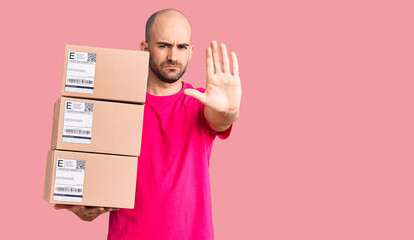 Young handsome man holding delivery package with open hand doing stop sign with serious and...