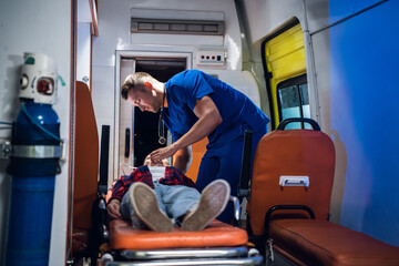 Unconscious woman lying on a stretcher in an ambulance car, a paramedic providing her first aid.