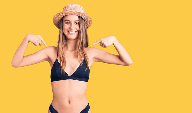 Young beautiful girl wearing bikini and hat looking confident with smile on face, pointing oneself with fingers proud and happy.