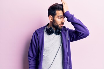 Fototapeta premium Young handsome man with beard listening to music using headphones surprised with hand on head for mistake, remember error. forgot, bad memory concept.