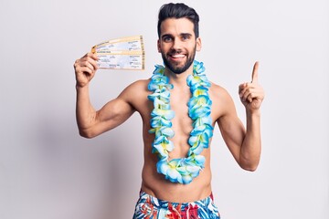 Young handsome man with beard wearing swimwear and hawaiian lei holding boarding pass smiling happy...