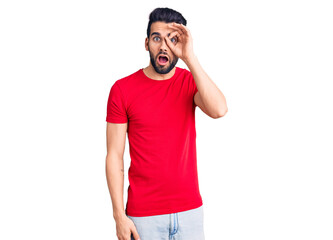 Young handsome man with beard wearing casual t-shirt doing ok gesture shocked with surprised face, eye looking through fingers. unbelieving expression.