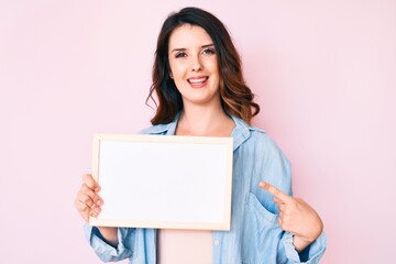 Young beautiful brunette woman holding blank empty banner smiling happy pointing with hand and finger