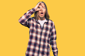 Handsome caucasian man with long hair wearing hipster shirt doing ok gesture shocked with surprised face, eye looking through fingers. unbelieving expression.