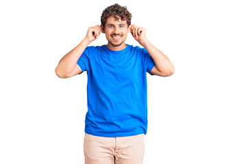 Young handsome man with curly hair wearing casual clothes smiling pulling ears with fingers, funny...