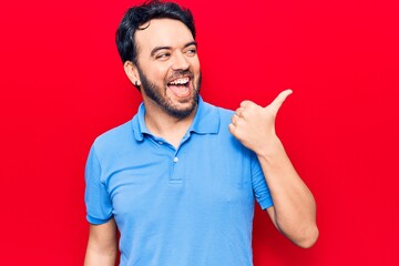 Young hispanic man wearing casual clothes pointing thumb up to the side smiling happy with open mouth