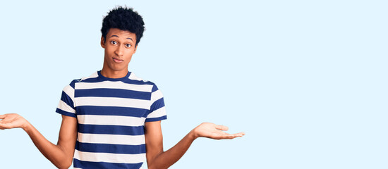 Young african american man wearing casual clothes clueless and confused expression with arms and hands raised. doubt concept.