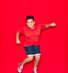 Adorable kid wearing casual clothes smiling happy. Jumping with smile on face over isolated red background