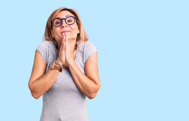 Young blonde woman wearing casual clothes praying with hands together asking for forgiveness smiling confident.