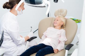 A satisfied little dentist patient showing her perfect smile after dental treatment in a clinic. A box with medical tools in the background.