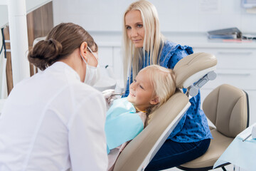 Obraz premium A female pediatric dental specialist going over the results of the girl's oral checkup with her mom. Dentist office.