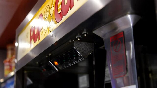Male hand pressing digital start stop button knob on metal surface of automatic popcorn making machine engine