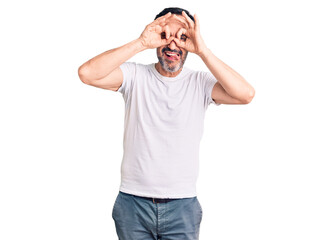 Middle age handsome man wearing casual t-shirt doing ok gesture like binoculars sticking tongue out, eyes looking through fingers. crazy expression.
