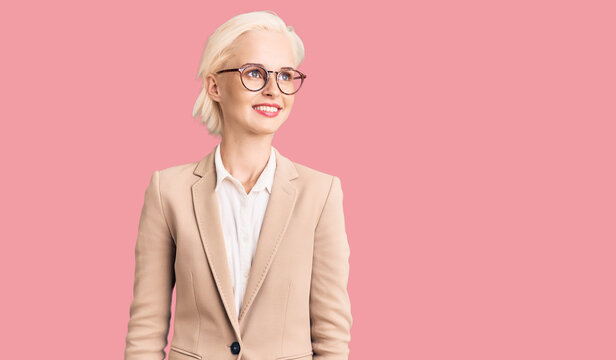 Young blonde woman wearing business clothes and glasses looking away to side with smile on face, natural expression. laughing confident.