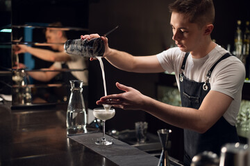 a young bartender makes a milk cocktail with a shaker on the bar.