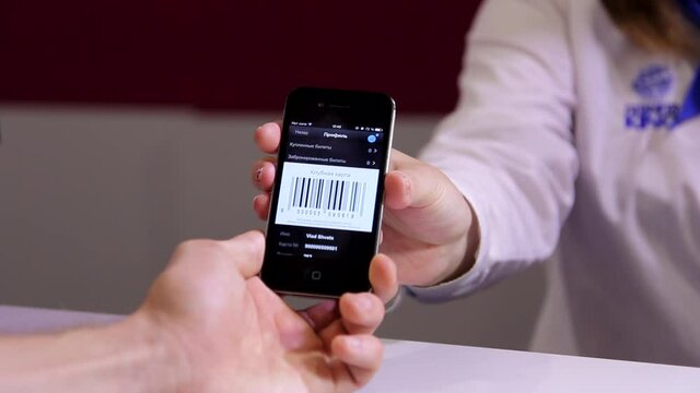 Woman cashier hand showing male customer a cell smart phone with cinema ticket barcode information in close up view