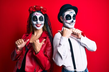 Couple wearing day of the dead costume over red pointing to the back behind with hand and thumbs up, smiling confident
