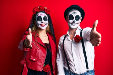 Couple wearing day of the dead costume over red smiling friendly offering handshake as greeting and welcoming. successful business.