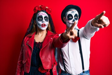 Couple wearing day of the dead costume over red pointing with finger surprised ahead, open mouth amazed expression, something on the front