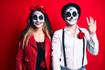 Couple wearing day of the dead costume over red showing and pointing up with fingers number four while smiling confident and happy.