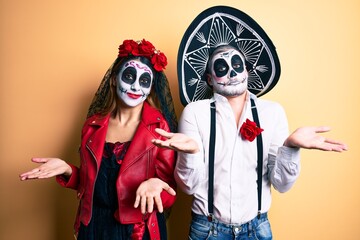 Couple wearing day of the dead costume over yellow clueless and confused expression with arms and hands raised. doubt concept.