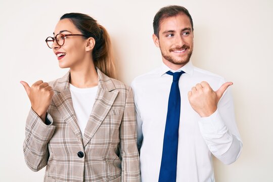 Beautiful couple wearing business clothes smiling with happy face looking and pointing to the side with thumb up.