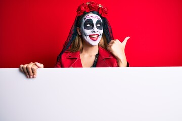 Woman wearing day of the dead costume holding blank empty banner pointing thumb up to the side smiling happy with open mouth
