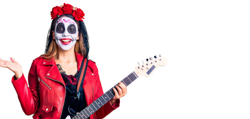 Obraz na płótnie Canvas Woman wearing day of the dead costume playing electric guitar celebrating victory with happy smile and winner expression with raised hands